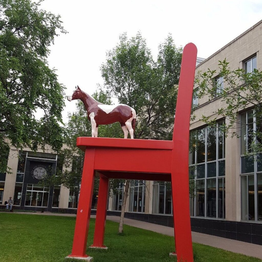 Large red chair with brown and white horse statue standing on top of it outside of Denver Central Library Branch