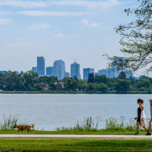 Two women walking a dog at Sloan's Lake, overlooking Downtown Denver.